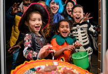 Children in Halloween costumes trick-or-treating at a doorstep with a basket of candy