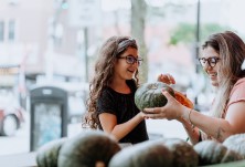 Mother and daughter, both wearing glasses, choose fresh produce at a local farmers market.